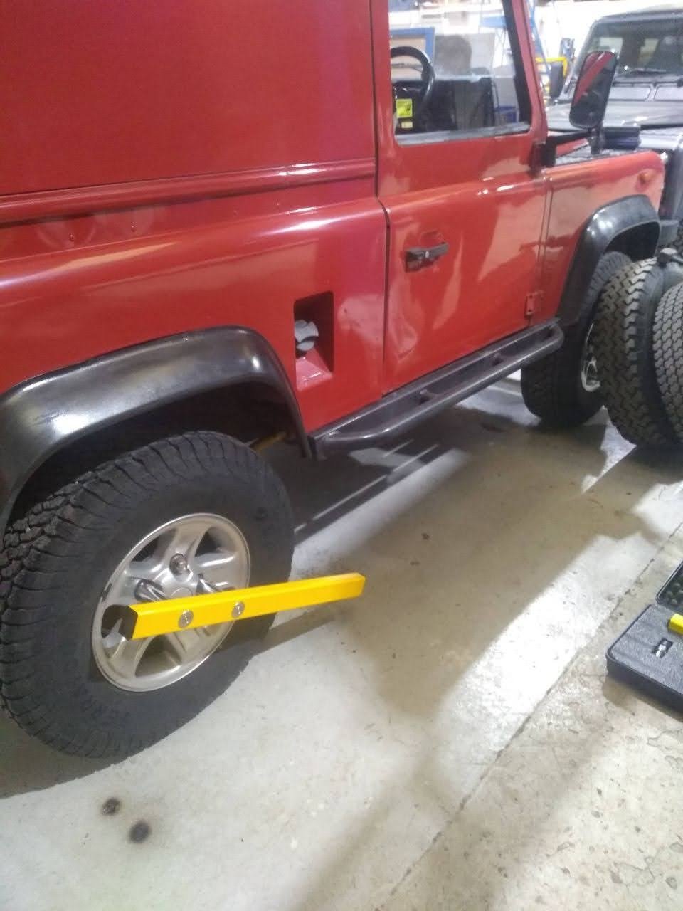 Red Land Rover Defender 4x4 secured with the yellow KLUNK wheel lock